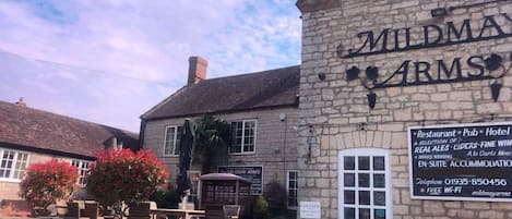 A stone building with a sign reading 'MILD MAY ARM'S' and a signboard advertising a restaurant, pub, and hotel.