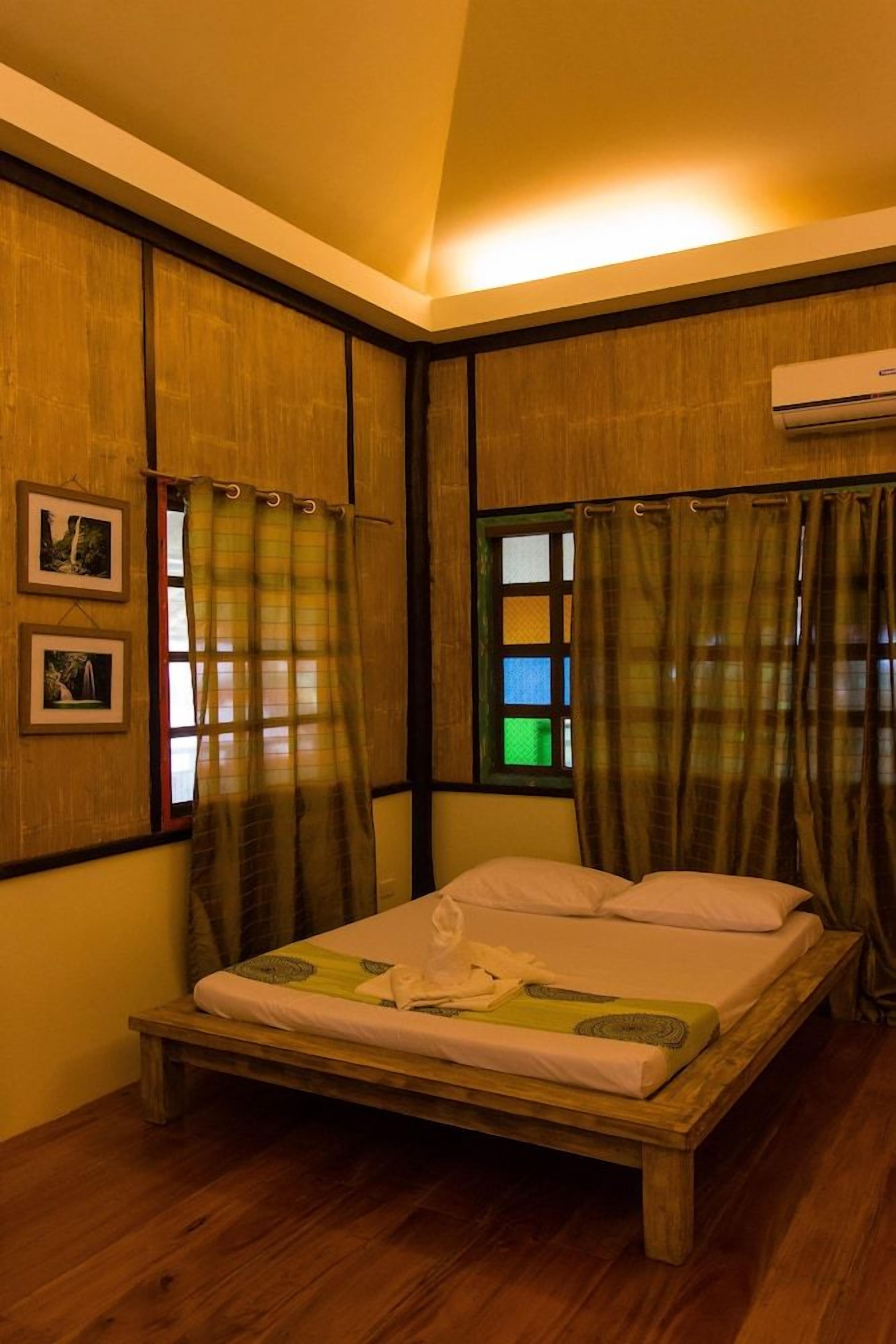 A room with a wooden bed, two windows with curtains, and an air conditioning unit.