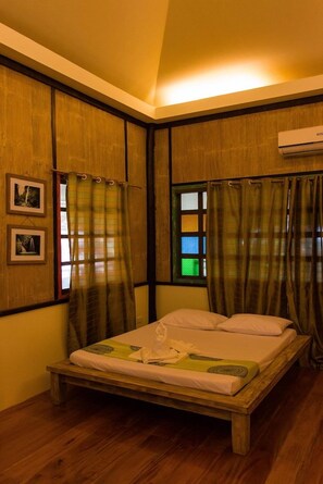 A room with a wooden bed, two windows with curtains, and an air conditioning unit.