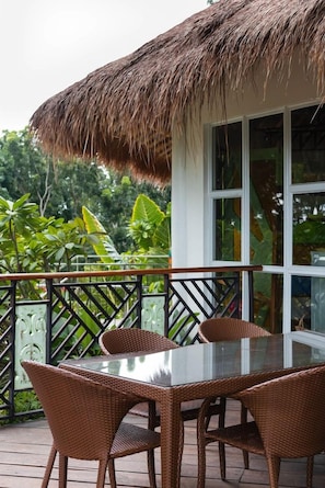 A glass-top table with wicker chairs, a thatched roof, and a view of lush greenery.