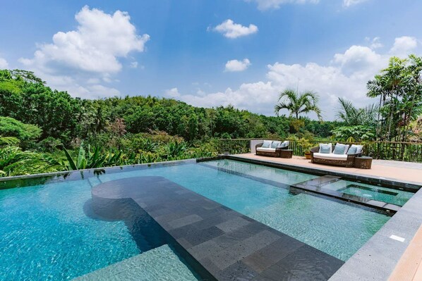 A rectangular infinity pool with clear water, surrounded by a wooden deck and two lounge chairs with cushions. - Damires Hills Tierra Verde (Janiuay)