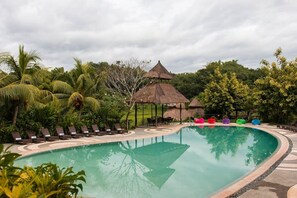A swimming pool with lounge chairs and a thatched-roof structure.