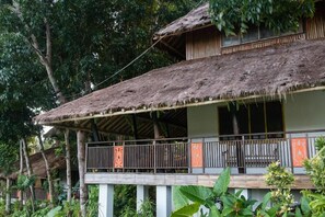 A traditional thatched-roof building with a balcony, surrounded by lush greenery.