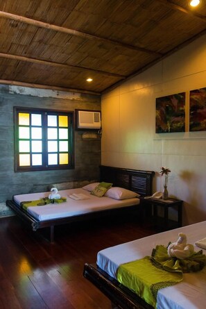 A room with two beds, a wooden ceiling, a window with a green frame, and a wall-mounted air conditioner.