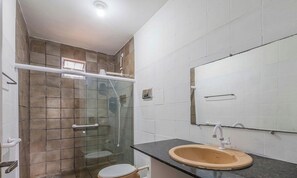 Ein Badezimmer mit Glasdusche, Toilette, Waschbecken in Beige sowie einem Spiegel an der Wand.