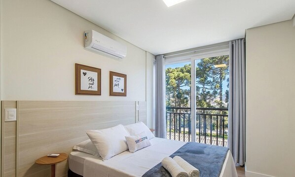 A hotel room with a bed, a small bedside table, a wall-mounted air conditioner, and two framed pictures. - Apt. w/ Priv. BBQ & City View Rod0304 (Canela)
