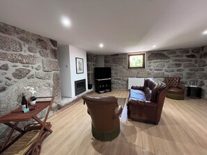 A stone-walled room with a fireplace, leather furniture, and a television. - Quinta de São Martinho – Pet-Friendly Country House in Gerês (Soengas)