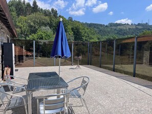 An outdoor patio with a table and chairs, a blue umbrella, and a view of a forested hillside. - Quinta de São Martinho – Pet-Friendly Country House in Gerês (Soengas)