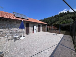 Ein Steinhaus mit einem Ziegeldach, einer Solaranlage, einer Glastür und einer Terrasse mit Tisch und Stühlen.