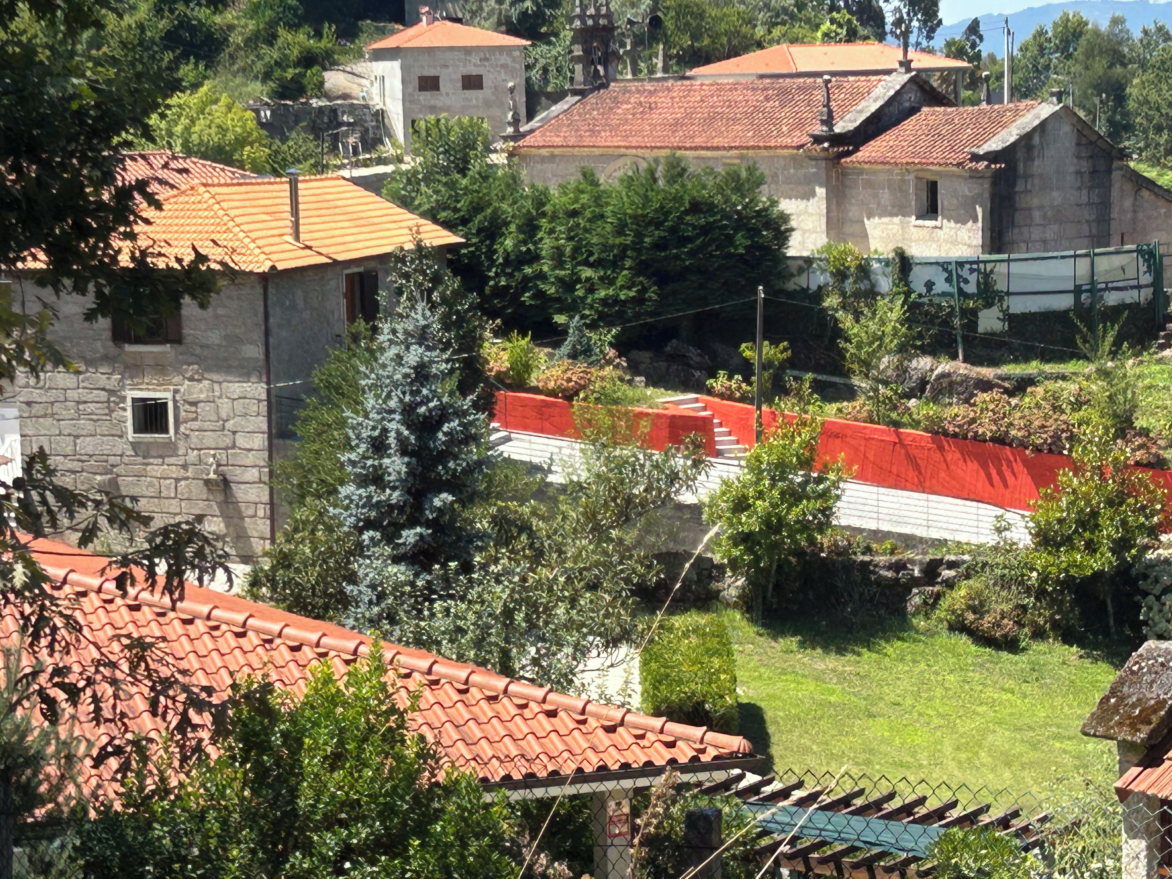 A residential area with stone buildings, red-tiled roofs, and a fenced garden area.