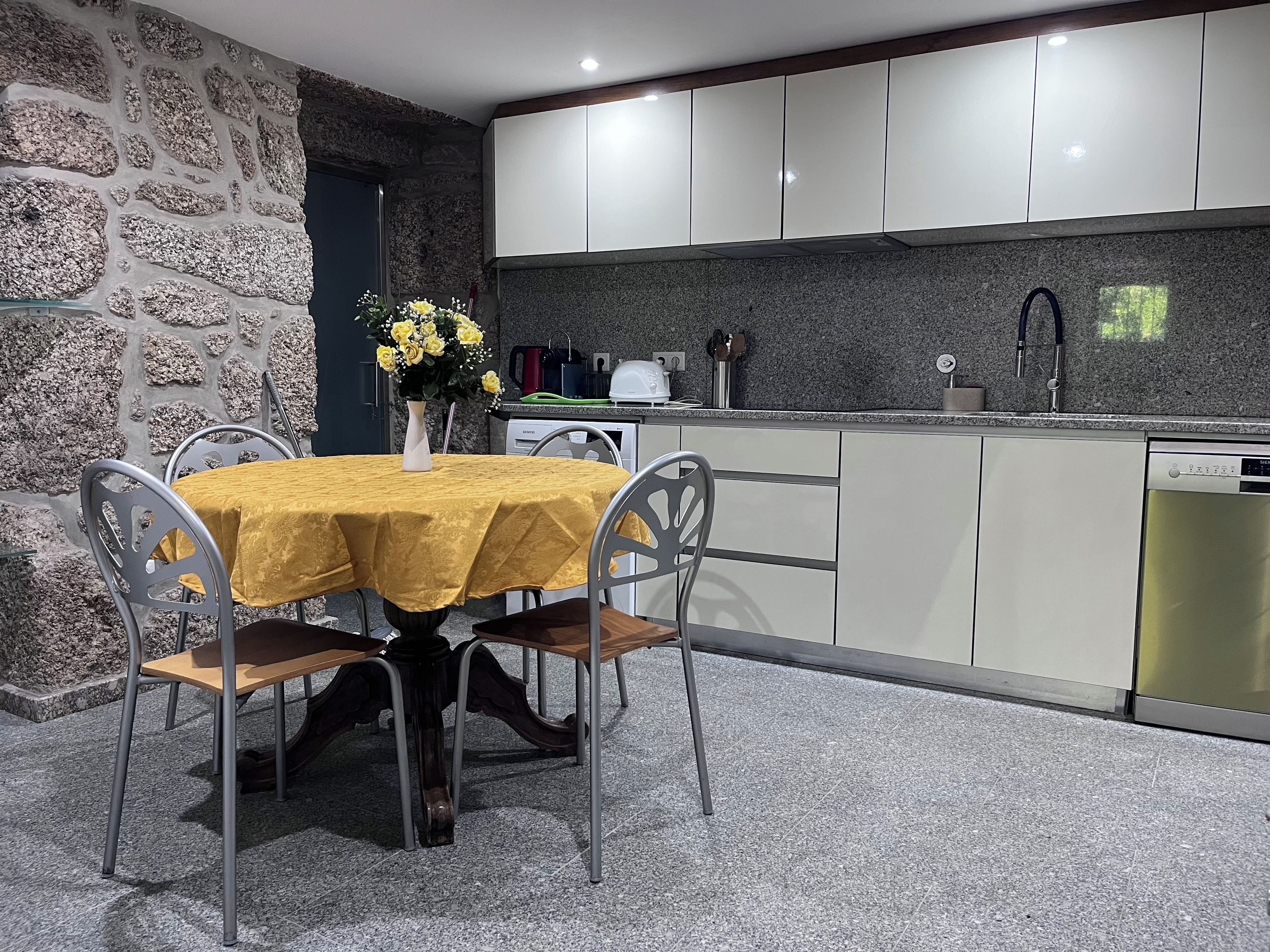 A modern kitchen with granite countertops, white cabinets, and a dining area with a yellow tablecloth.
