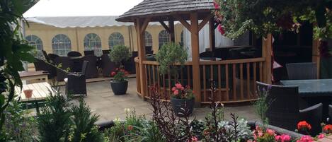 An outdoor patio area with a gazebo, seating arrangements, and potted plants.