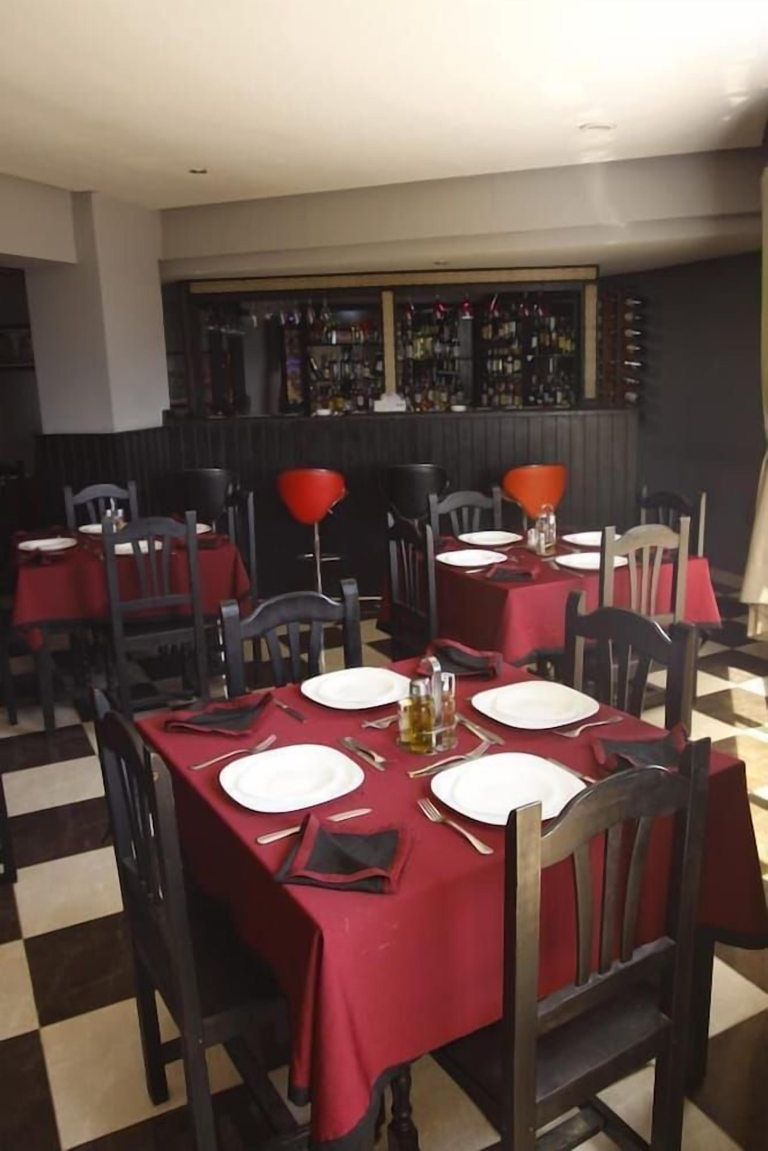 Un restaurante con mesas dispuestas para comer, con manteles rojos y sillas negras.