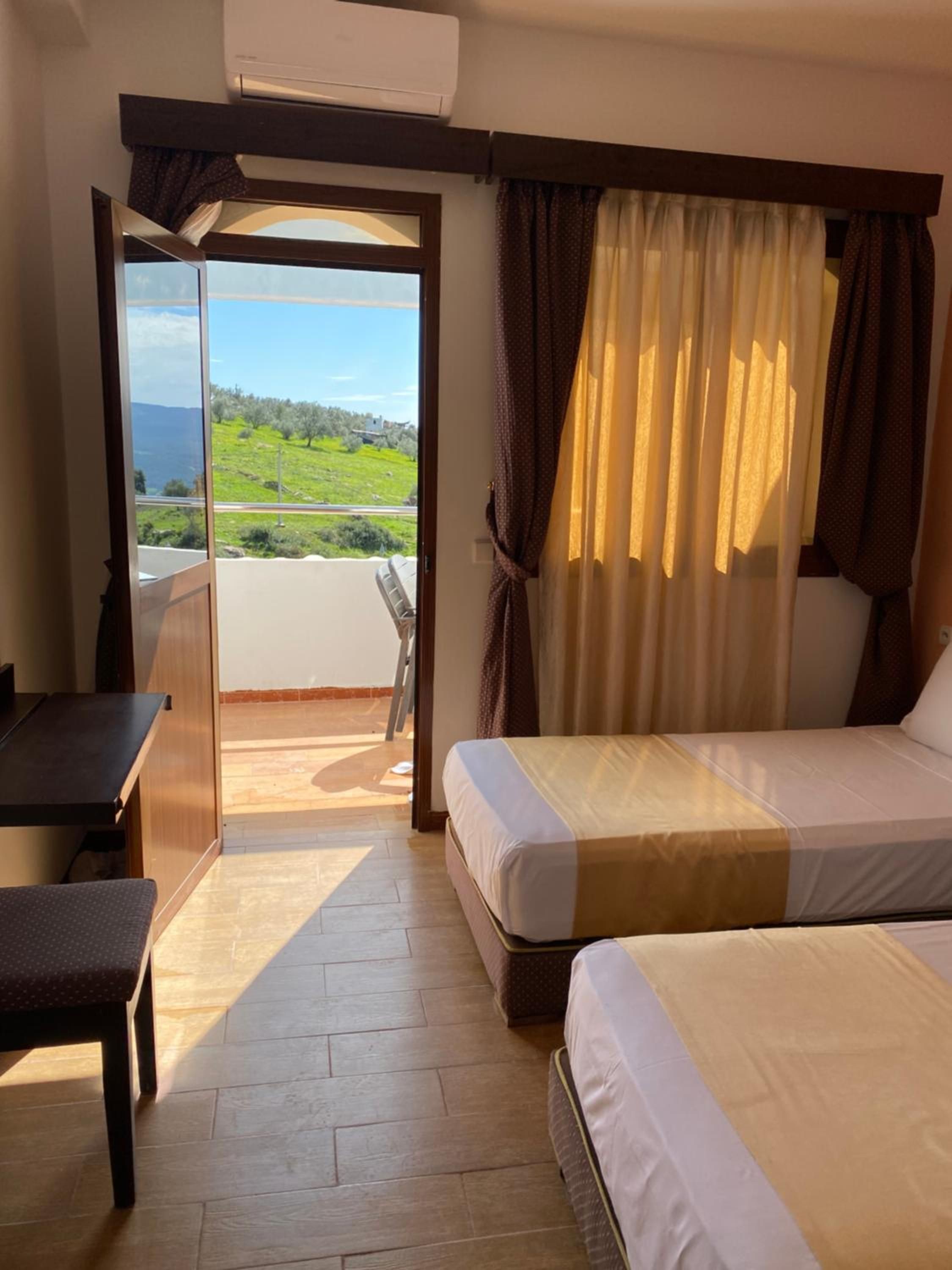 Habitación de hotel con cama, escritorio y vista a un paisaje verde a través de una puerta abierta.