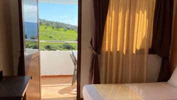 Habitación de hotel con cama, escritorio y vista a un paisaje verde a través de una puerta abierta.
