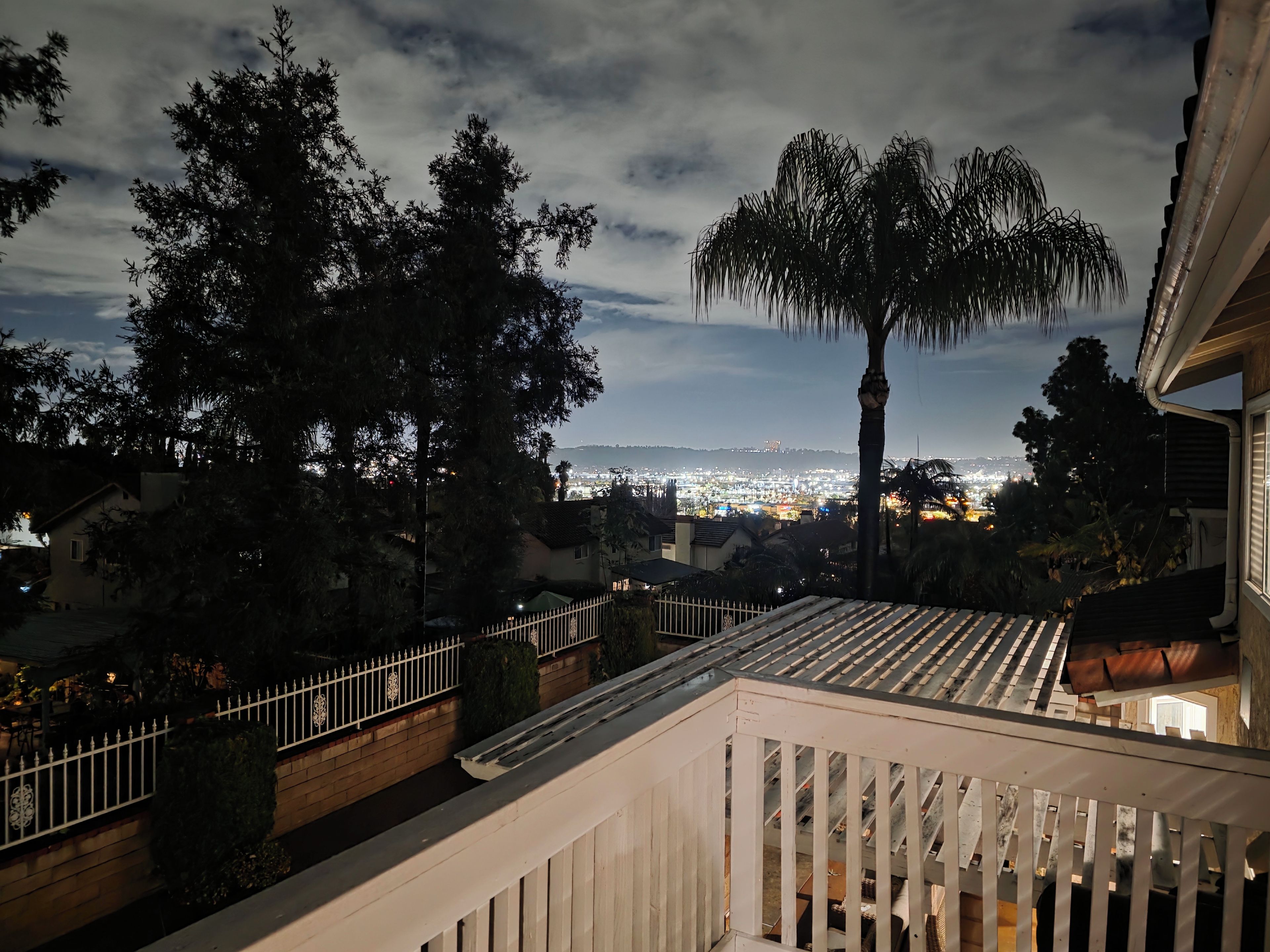 Un balcon offrant une vue sur le paysage urbain au crépuscule, avec un palmier et une balustrade.