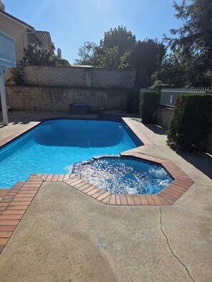 A rectangular swimming pool with a tiled edge, surrounded by a concrete deck and a brick border.