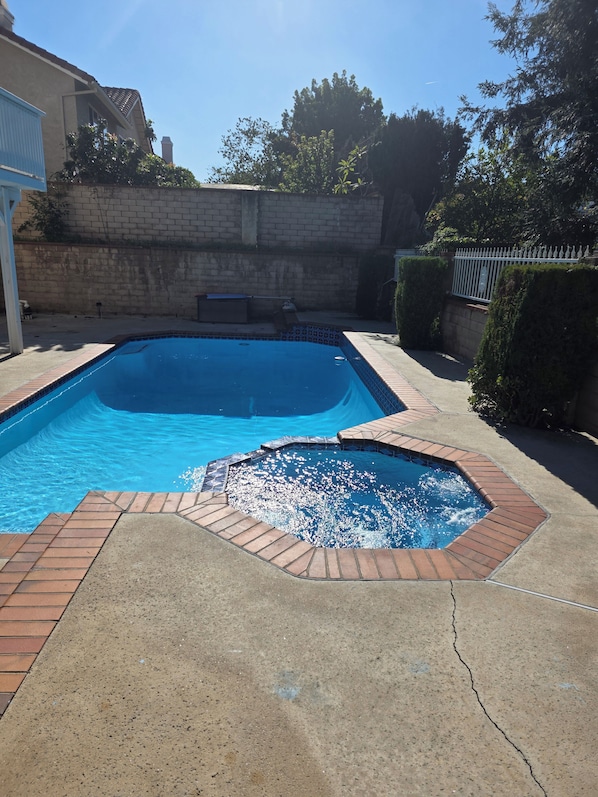 A rectangular swimming pool with a tiled edge, surrounded by a concrete deck and a brick border.