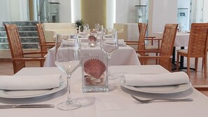 A dining table set with white tablecloth, plates, cutlery, and wine glasses, with a decorative shell centerpiece. - Akrogiali Boutique Hotel (Kassandra)