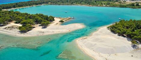 An aerial view of a coastal area with clear turquoise waters, sandy beaches, and dense green forests.