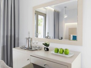 A hotel room with a white dresser, a mirror, a tray with a glass, and three green apples on a plate. - Akrogiali Boutique Hotel (Kassandra)
