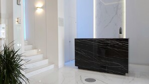 A modern reception area with a marble staircase, a black marble reception desk, and a potted plant. - Akrogiali Boutique Hotel (Kassandra)