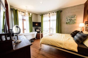 A hotel room with a bed, a vanity with a mirror, a bathtub, and a television. - Roomquest Rimrabeang At Amphawa (Amphawa)