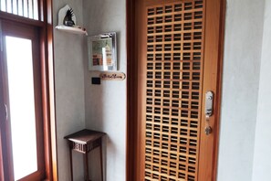 A room with a wooden door, a small table, a framed picture, and a shelf with decorative items. - Roomquest Rimrabeang At Amphawa (Amphawa)