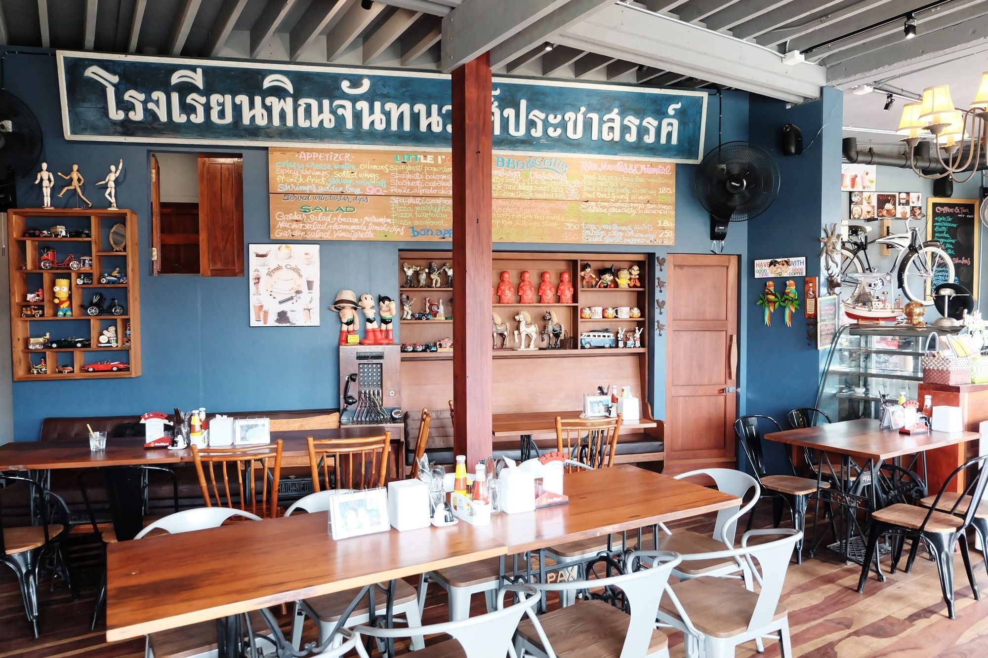 A restaurant interior with wooden tables and chairs, a menu board, and various decorations including figurines and wall art.
