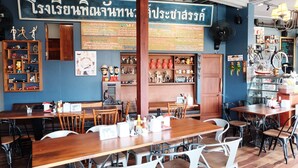 A restaurant interior with wooden tables and chairs, a menu board, and various decorations including figurines and a bicycle. - Roomquest Rimrabeang At Amphawa (Amphawa)