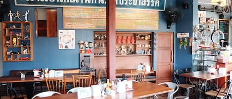Interior de restaurante con mesas y sillas de madera, un tablero de menú y diversas decoraciones, incluyendo figuritas y obras de arte en la pared.