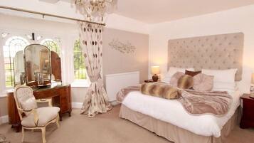 A bedroom with a large bed, a vanity with a mirror, a chair, and a chandelier.