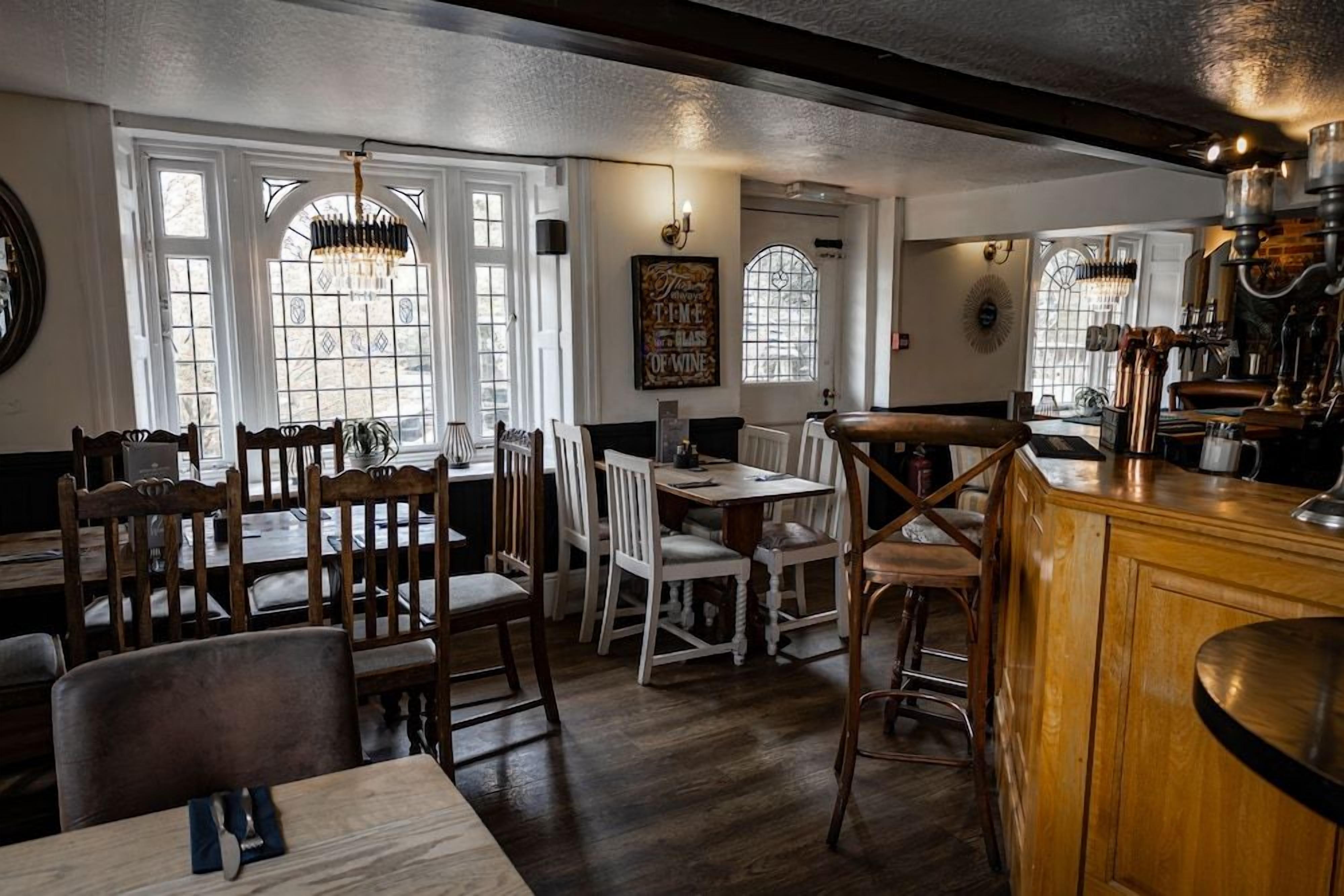A restaurant interior with wooden furniture, a bar area, and large windows allowing natural light.