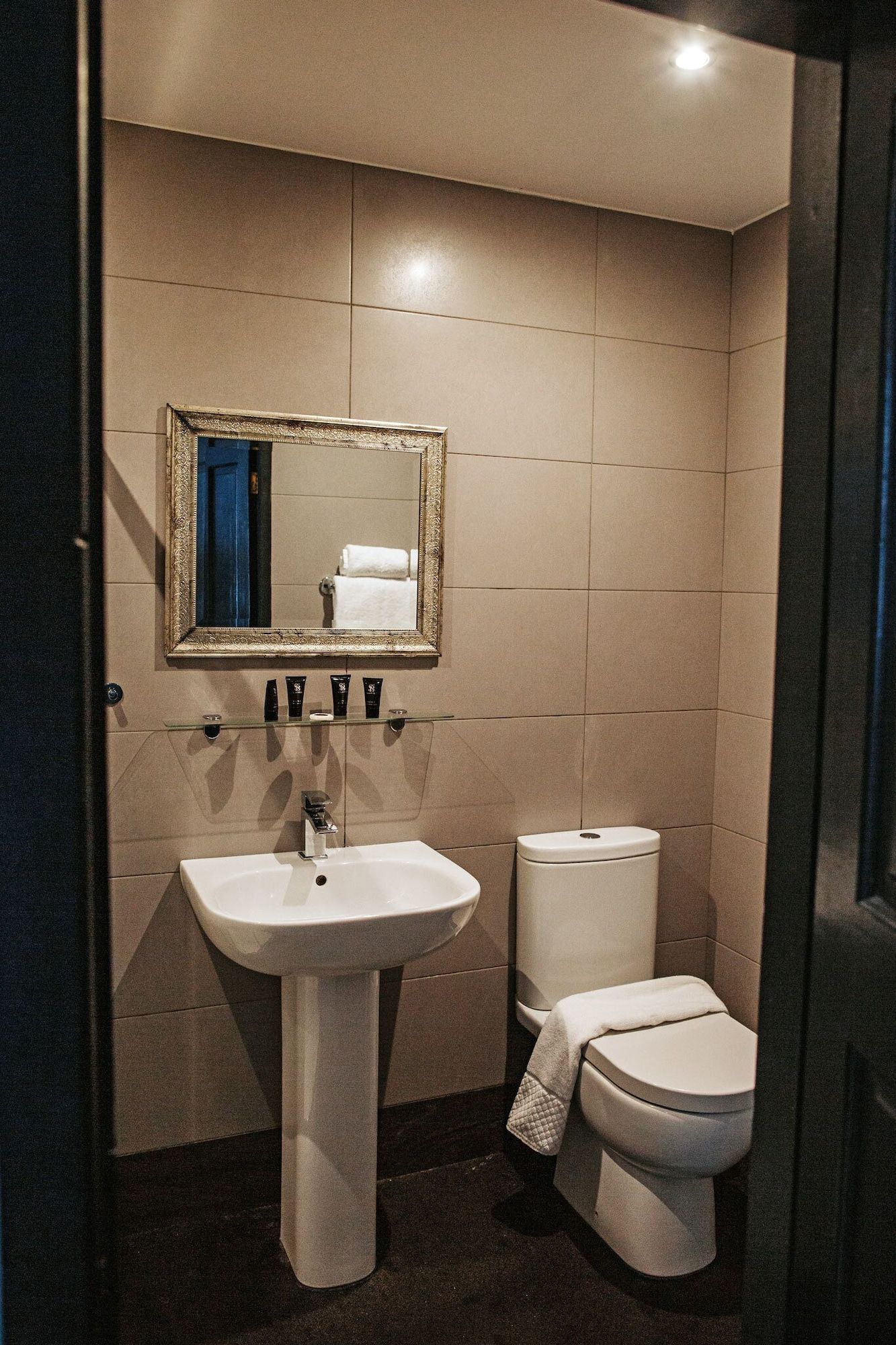 A bathroom with a pedestal sink, a toilet, and a mirror with a decorative frame.