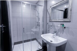 Un bagno moderno con doccia vetro, lavandino bianco e specchio con cornice decorativa.