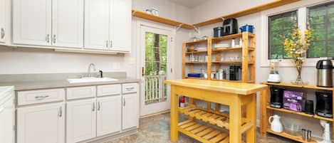Una cocina con armarios blancos, una mesa de madera y un ventanal con vista a follaje.