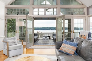 A spacious room with a large glass door leading to a deck, a grey sofa with patterned cushions, and a wooden coffee table. - Lakefront, Hot Tub, Dock, Kayaks, SUPs, Games, Fire pit (Boydton)