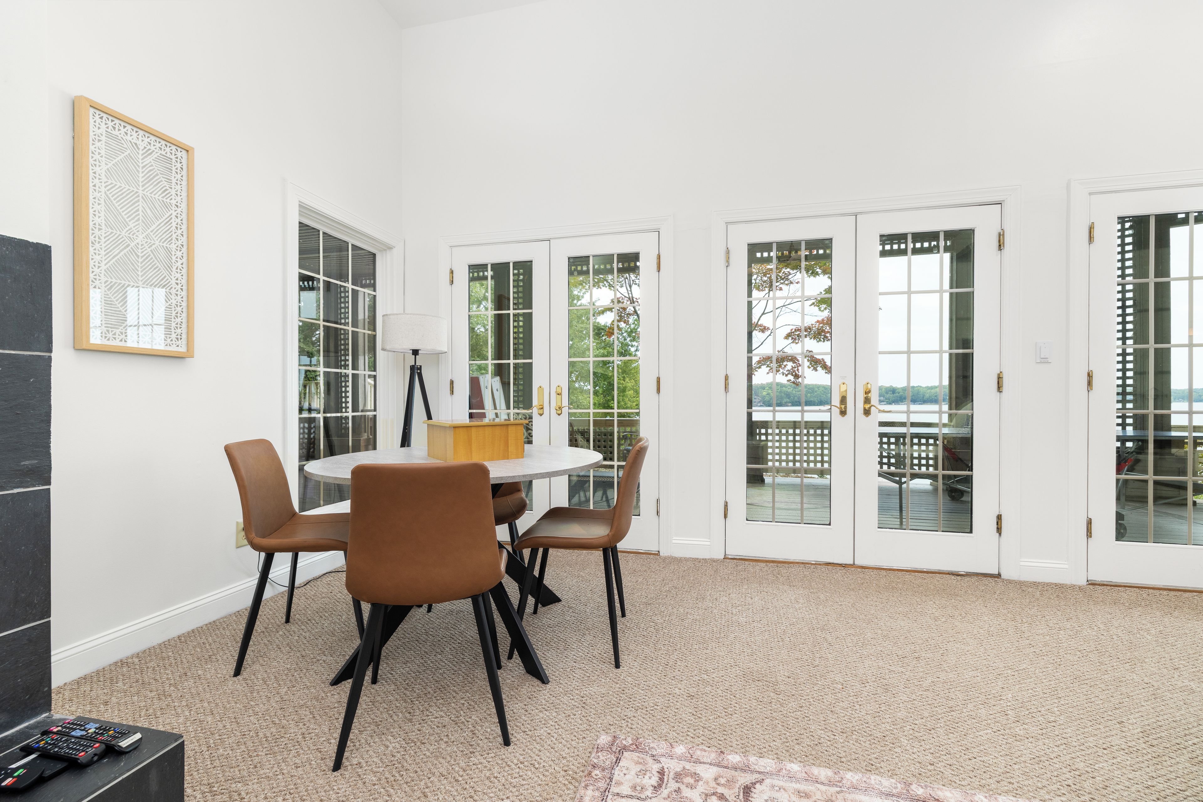 A dining area with a round table and chairs, a lamp, and a view through glass doors to an outdoor deck.
