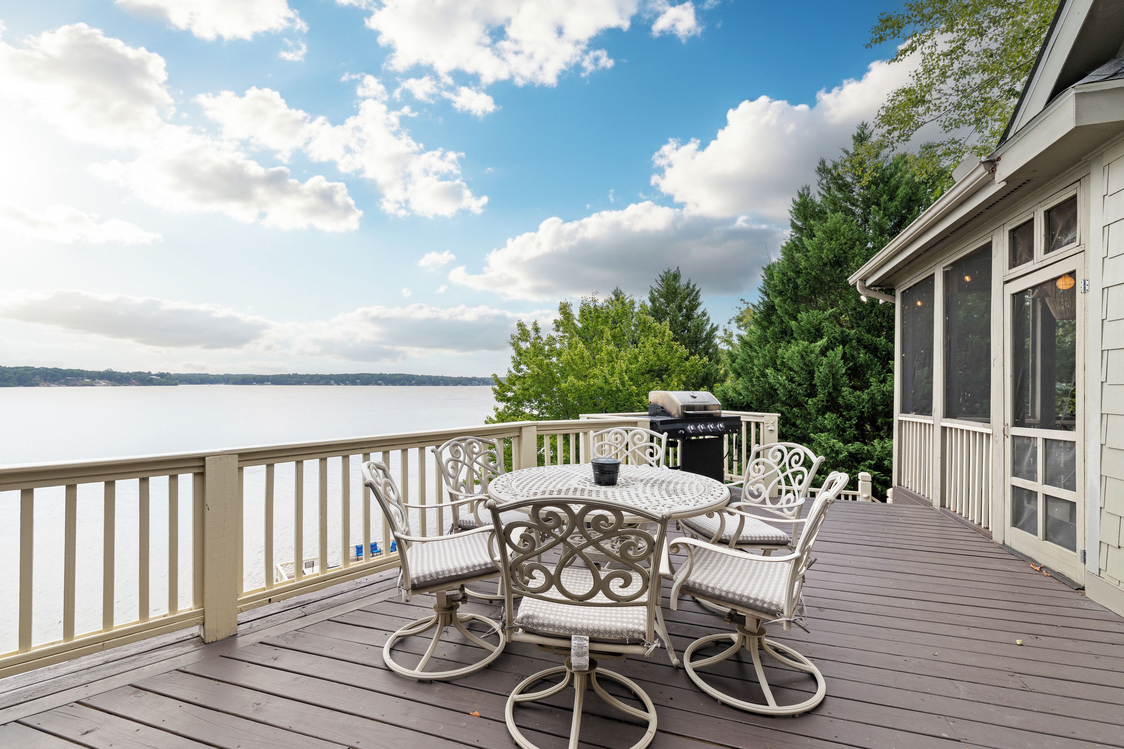 A deck with outdoor furniture and a grill, overlooking a body of water.