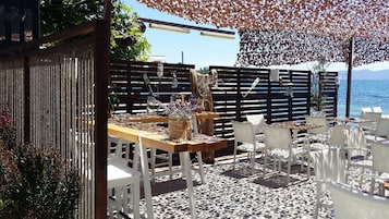 An outdoor seating area with tables and chairs, a decorative fence, and a view of the sea.