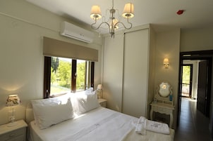 A bedroom with a bed, bedside lamps, a mirror, a nightstand, and a window with a view of greenery.