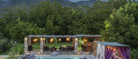 A pool area with lounge chairs, a stone structure with lights, and a seating area with a view of the mountains.