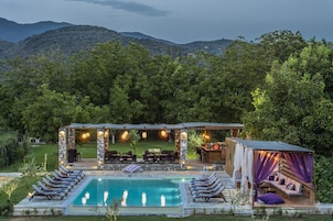 A pool area with lounge chairs, a stone structure with lights, and a seating area with a view of the mountains.