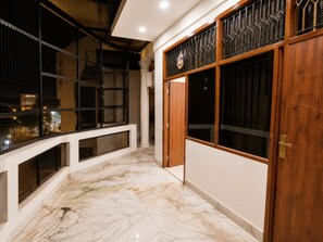 A corridor with a marble floor, a wooden door, and a window with a decorative grille.