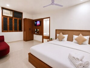 A hotel room with a bed, a red chair, a wardrobe, a television, and a ceiling fan.