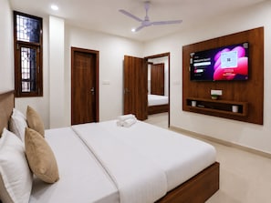 Quarto de hotel com uma cama, televisão na parede e ventilador de teto.