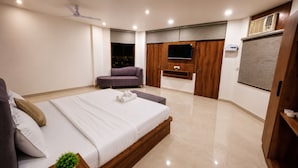 A modern bedroom with a large bed, a sofa, a TV, and a ceiling fan. - ZenithSuites - Vrindavan (Vrindavan)