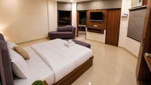 A modern bedroom with a large bed, a seating area, a TV, and a balcony with a city view. - ZenithSuites - Vrindavan (Vrindavan)