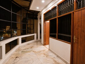 A corridor with a marble floor, a wooden door, and a window with a metal grill.
