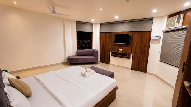 A modern hotel room with a large bed, a seating area, and a TV mounted on the wall. - ZenithSuites - Vrindavan (Vrindavan)